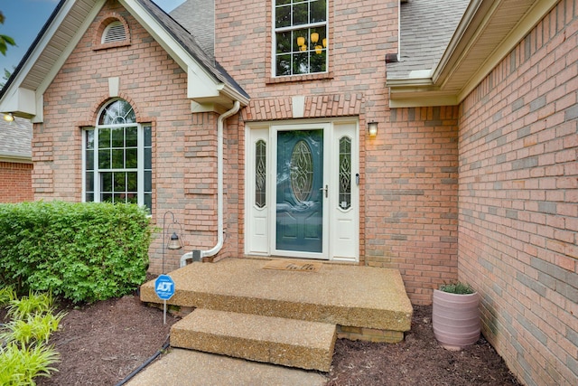doorway to property featuring brick siding and roof with shingles