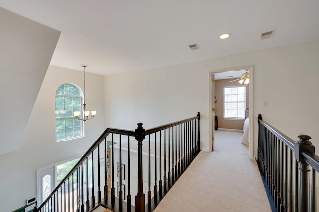hallway with an upstairs landing, a chandelier, plenty of natural light, light colored carpet, and recessed lighting