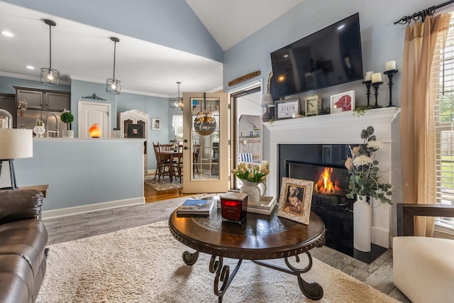 living room with wood finished floors, vaulted ceiling, a glass covered fireplace, ornamental molding, and baseboards