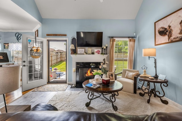 living room featuring lofted ceiling, baseboards, a fireplace with flush hearth, and wood finished floors