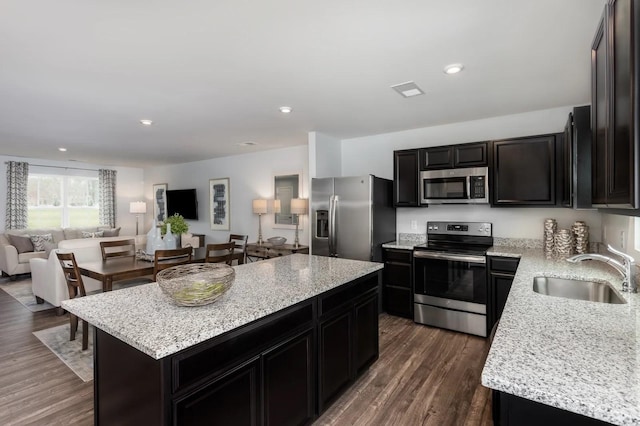 kitchen featuring appliances with stainless steel finishes, a sink, open floor plan, a center island, and dark wood-style flooring