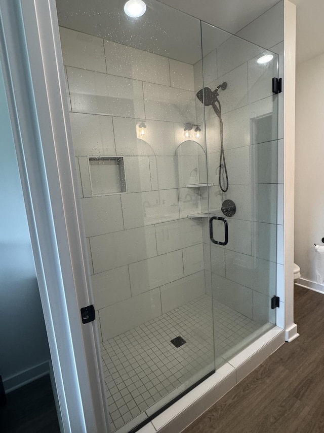 full bath featuring wood finished floors, a shower stall, toilet, and baseboards