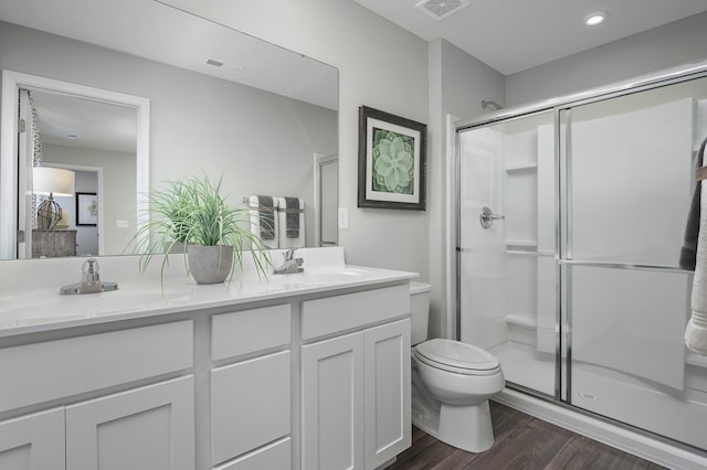 bathroom with wood finished floors, toilet, a stall shower, double vanity, and recessed lighting