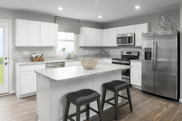 kitchen featuring appliances with stainless steel finishes, a sink, a kitchen bar, white cabinets, and recessed lighting
