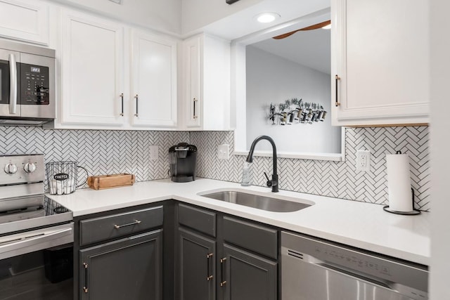 kitchen with stainless steel appliances, a sink, white cabinetry, and light countertops