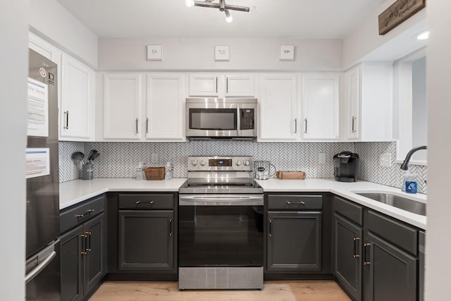 kitchen with appliances with stainless steel finishes, a sink, white cabinets, and light countertops