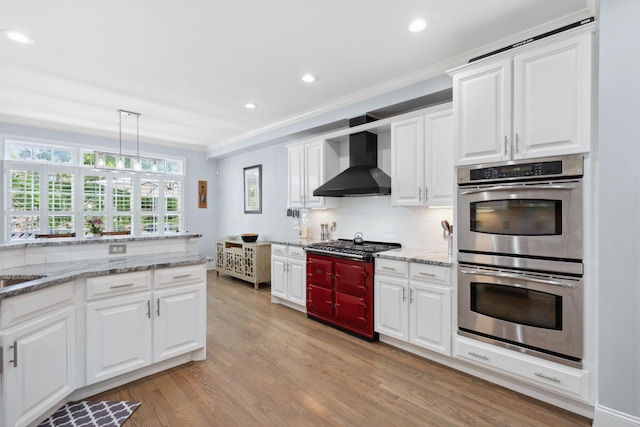 9702 Amethyst Ln, Brentwood, TN 37027 - kitchen featuring stainless steel appliances, wall chimney exhaust hood, crown molding, light wood-style floors, and tasteful backsplash