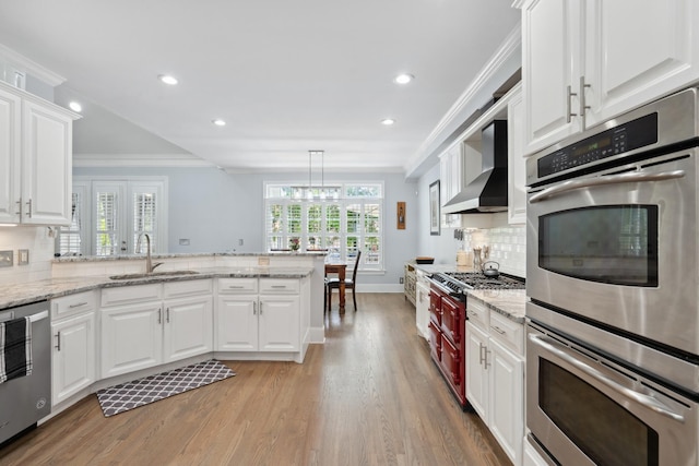 9702 Amethyst Ln, Brentwood, TN 37027 - kitchen featuring a sink, wall chimney range hood, stainless steel appliances, a peninsula, and light wood finished floors