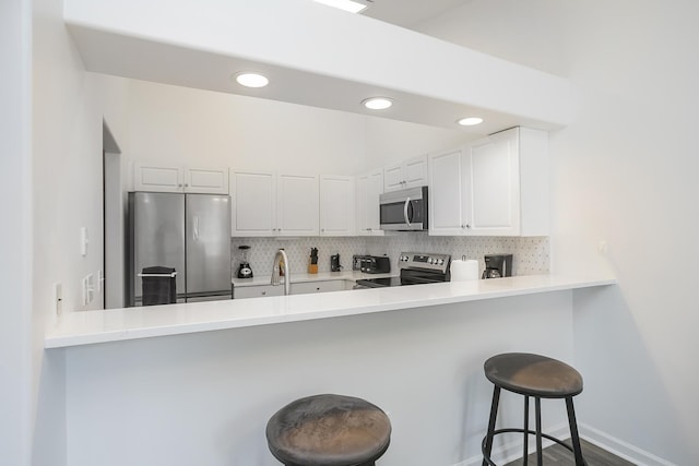 kitchen with stainless steel appliances, a peninsula, tasteful backsplash, white cabinets, and recessed lighting