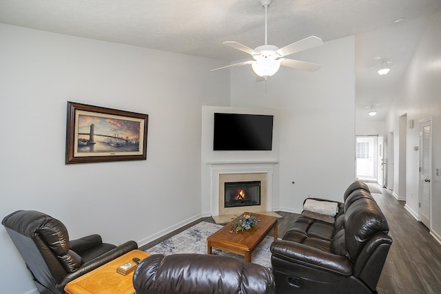 living room with dark wood-type flooring, a ceiling fan, a fireplace with flush hearth, and baseboards