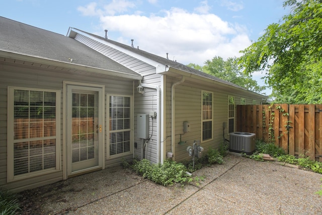 rear view of house with central AC unit, fence, a patio area, and a shingled roof