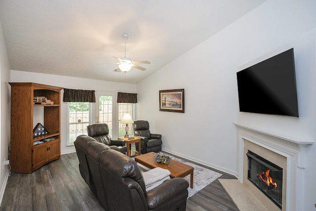 living area featuring lofted ceiling, ceiling fan, a fireplace, dark wood finished floors, and baseboards