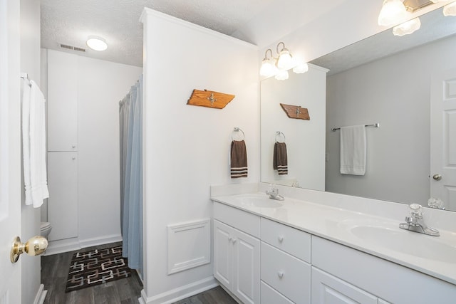 bathroom featuring wood finished floors, double vanity, a textured ceiling, baseboards, and a shower with shower curtain