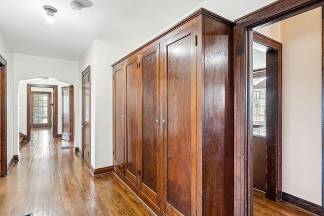 hallway featuring arched walkways, wood finished floors, and baseboards