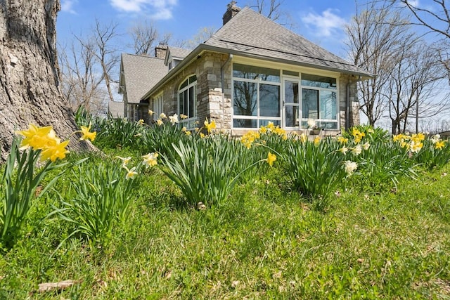view of side of property with a chimney, stone siding, a sunroom, and a shingled roof