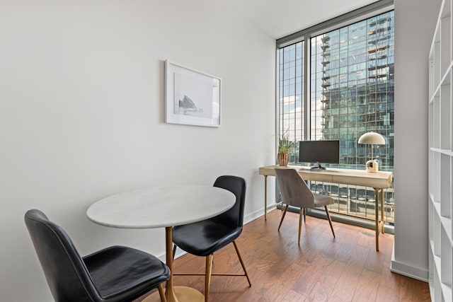 office area featuring floor to ceiling windows, wood finished floors, and baseboards