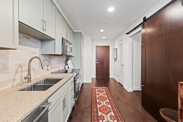 kitchen featuring appliances with stainless steel finishes, a sink, light stone counters, dark wood-style flooring, and tasteful backsplash