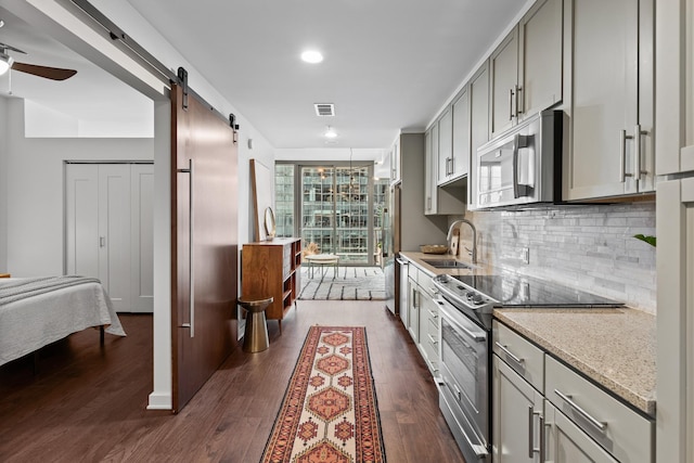 kitchen with appliances with stainless steel finishes, a barn door, gray cabinetry, a sink, and tasteful backsplash