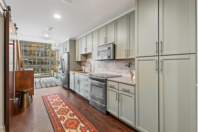 kitchen featuring stainless steel appliances, a sink, gray cabinets, decorative backsplash, and dark wood finished floors
