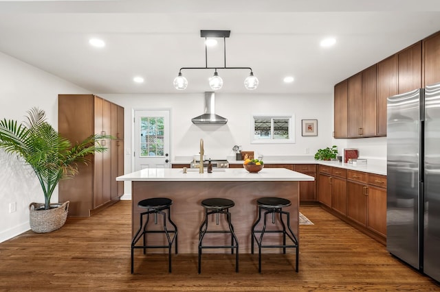 kitchen featuring stainless steel refrigerator, light countertops, wood finished floors, a kitchen bar, and recessed lighting