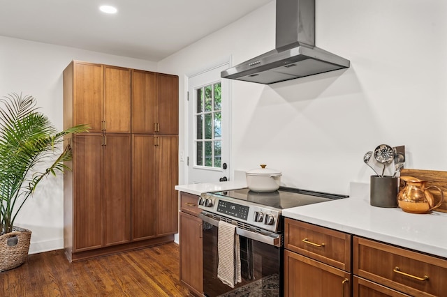 kitchen with electric stove, wall chimney range hood, dark wood finished floors, light countertops, and brown cabinets