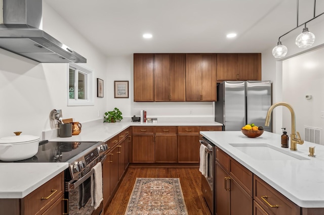 kitchen featuring appliances with stainless steel finishes, wall chimney exhaust hood, dark wood finished floors, a sink, and light countertops