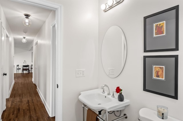 half bath featuring wood finished floors, a sink, toilet, and baseboards