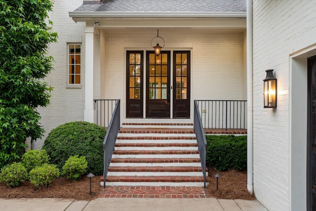 entrance to property with brick siding, roof with shingles, and covered porch