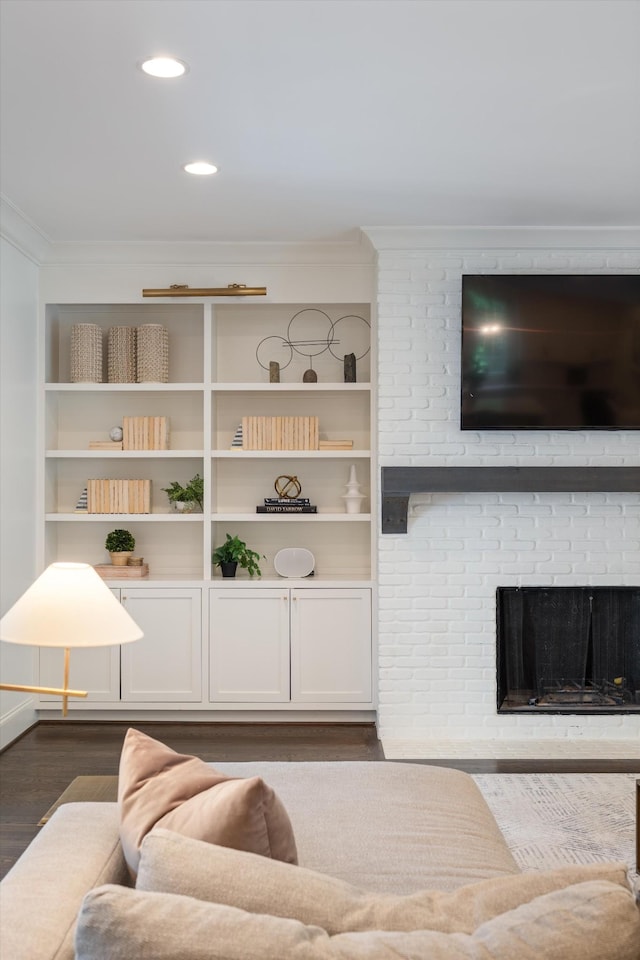 living area featuring crown molding, dark wood-style floors, built in shelves, recessed lighting, and a brick fireplace