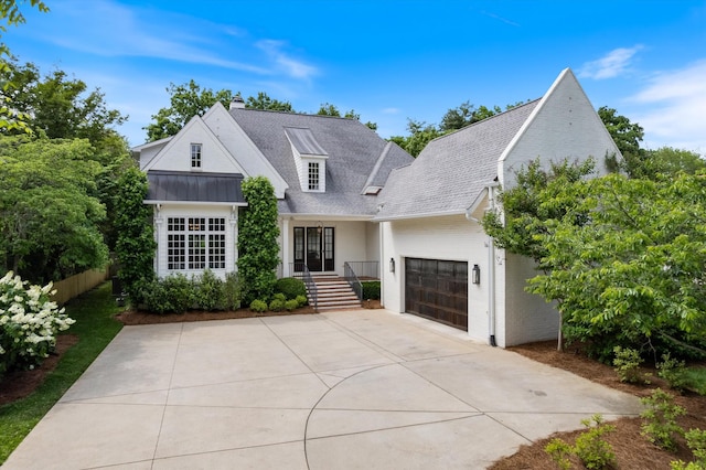 modern farmhouse with a garage, driveway, a chimney, fence, and a standing seam roof