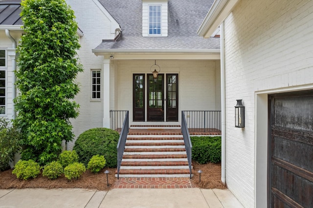 entrance to property with a shingled roof, brick siding, and a porch