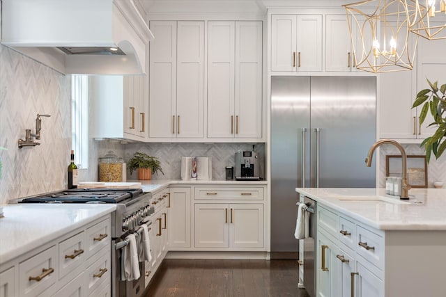 kitchen with high quality appliances, premium range hood, white cabinetry, decorative backsplash, and a sink