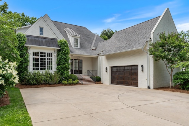 modern farmhouse style home featuring driveway, a shingled roof, a garage, brick siding, and a standing seam roof