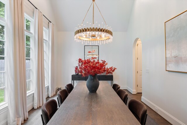 dining space featuring a chandelier, arched walkways, healthy amount of natural light, high vaulted ceiling, and baseboards