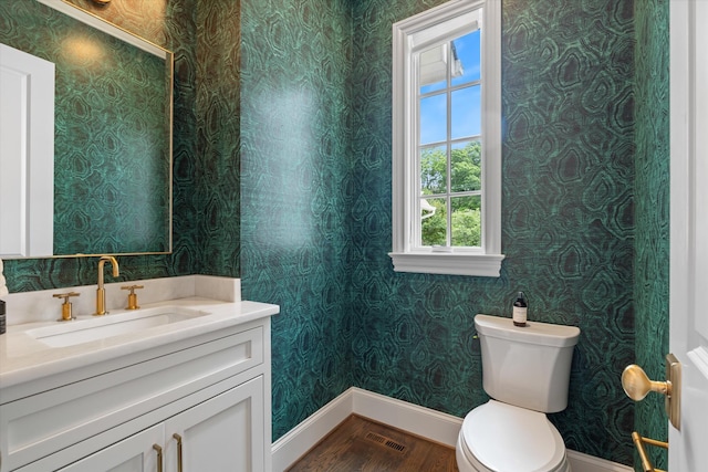 half bathroom featuring baseboards, wood finished floors, toilet, vanity, and wallpapered walls