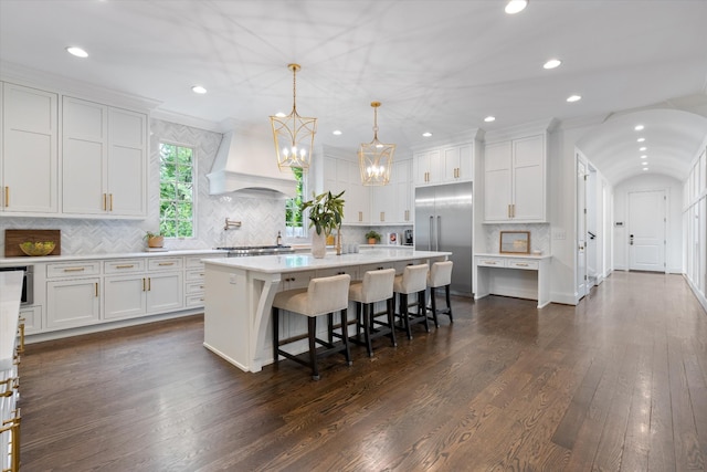 kitchen with stainless steel built in refrigerator, custom range hood, white cabinets, recessed lighting, and ornamental molding