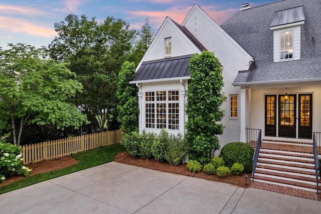 view of front of house with fence, a shingled roof, a standing seam roof, a patio, and brick siding