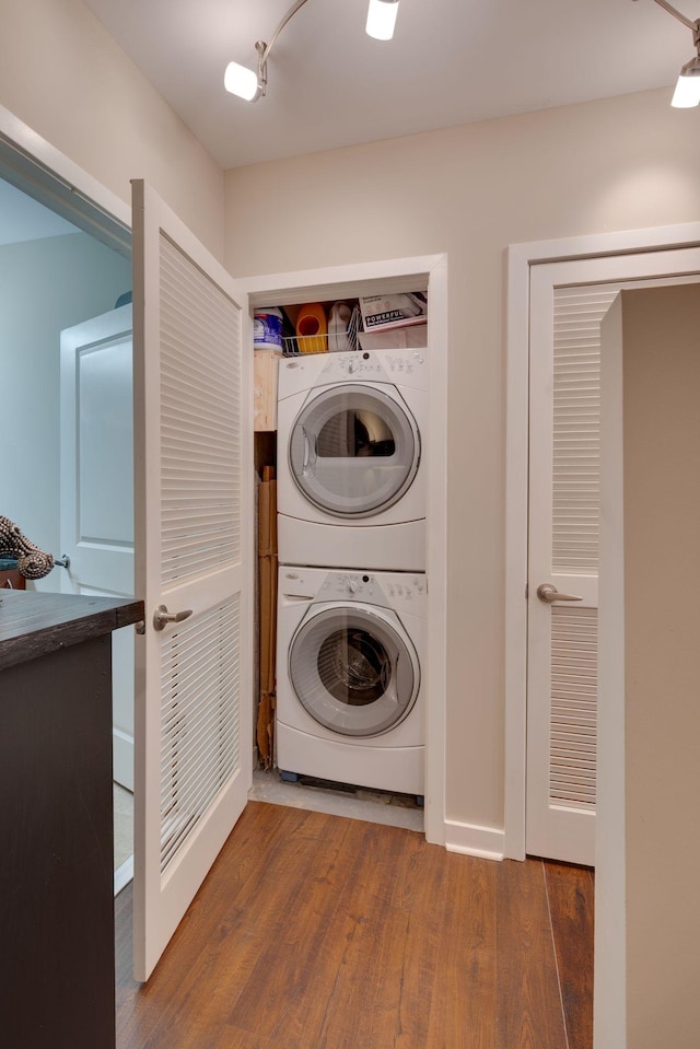clothes washing area with stacked washer / drying machine and wood finished floors