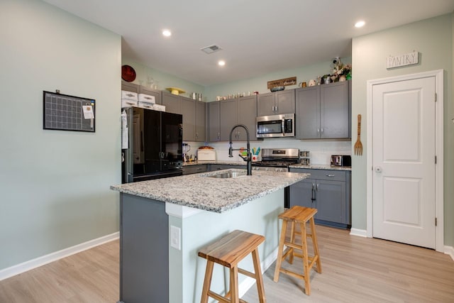 1017 Village Ct, Burns, TN 37029 - kitchen with stainless steel appliances, a sink, gray cabinets, light wood-style flooring, and a kitchen breakfast bar