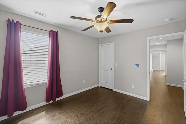 unfurnished bedroom featuring baseboards, dark wood finished floors, arched walkways, and ceiling fan