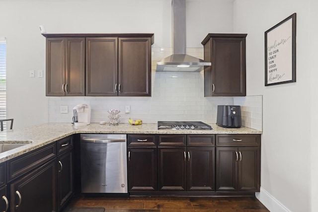 kitchen featuring appliances with stainless steel finishes, wall chimney exhaust hood, tasteful backsplash, light stone counters, and dark wood-style floors
