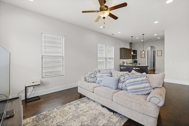 living area featuring arched walkways, dark wood-type flooring, a ceiling fan, baseboards, and recessed lighting