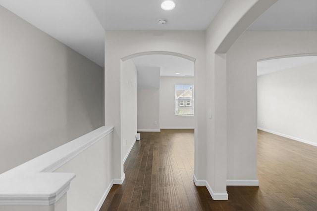 corridor with arched walkways, hardwood / wood-style floors, and baseboards