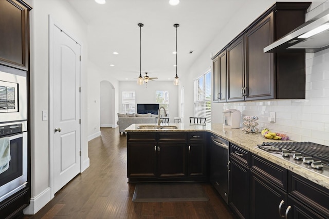 kitchen featuring a sink, appliances with stainless steel finishes, a peninsula, tasteful backsplash, and arched walkways