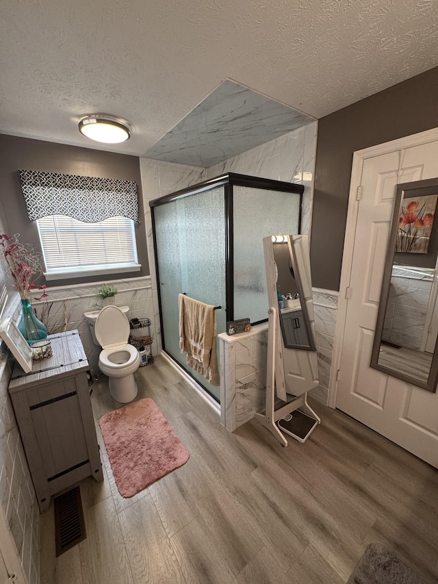 162 Pigeon Roost Rd, Brush Creek, TN 38547 - bathroom featuring a textured ceiling, wood finished floors, a shower stall, tile walls, and toilet