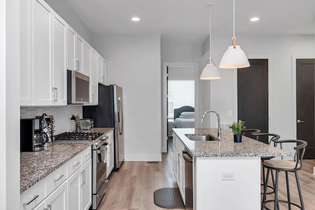 kitchen featuring a sink, appliances with stainless steel finishes, a breakfast bar, decorative backsplash, and a kitchen island with sink