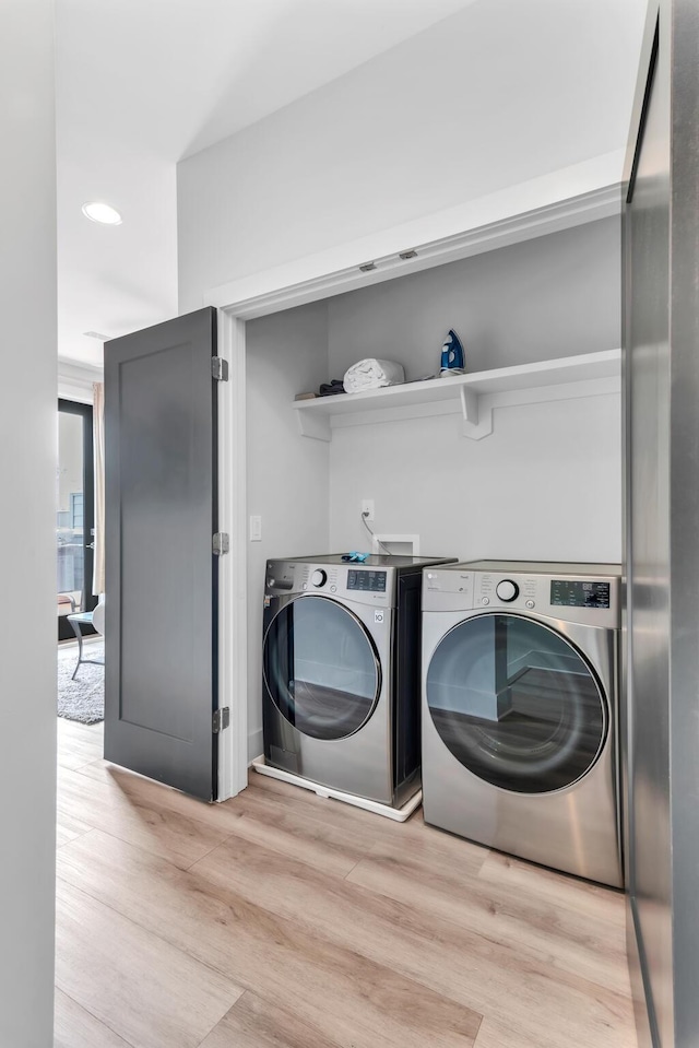 laundry area with washing machine and clothes dryer and light wood-type flooring