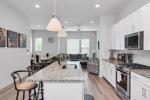 kitchen with stainless steel appliances, a sink, a kitchen breakfast bar, open floor plan, and light wood-style floors