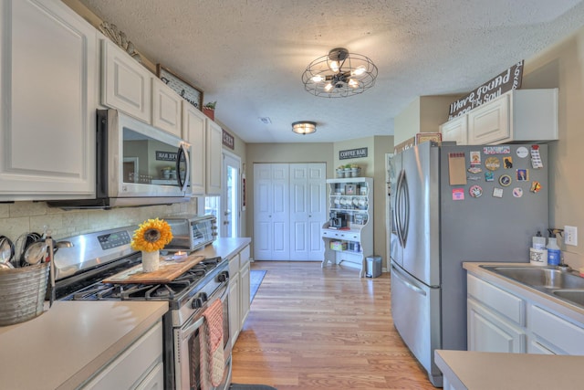 1753 Stone Hollow Ct, Hermitage, TN 37076 - kitchen with appliances with stainless steel finishes, a textured ceiling, white cabinetry, light wood-type flooring, and backsplash