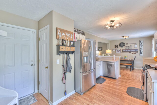 1753 Stone Hollow Ct, Hermitage, TN 37076 - kitchen with appliances with stainless steel finishes, a peninsula, light wood-style floors, a textured ceiling, and light countertops